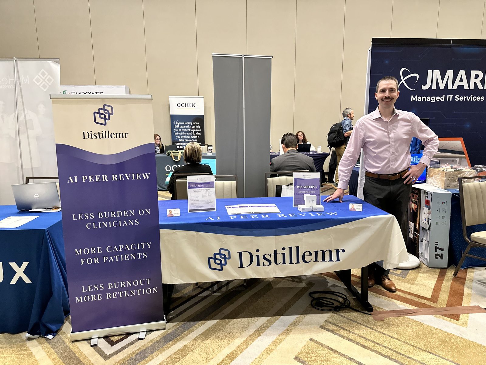 Paulius Mui, MD at the Distillemr booth, talking with FQHC leaders about AI peer review.